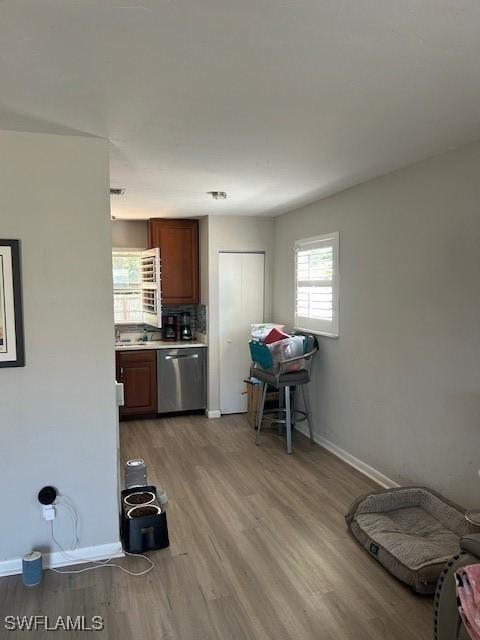 kitchen featuring baseboards, light countertops, stainless steel dishwasher, decorative backsplash, and light wood finished floors