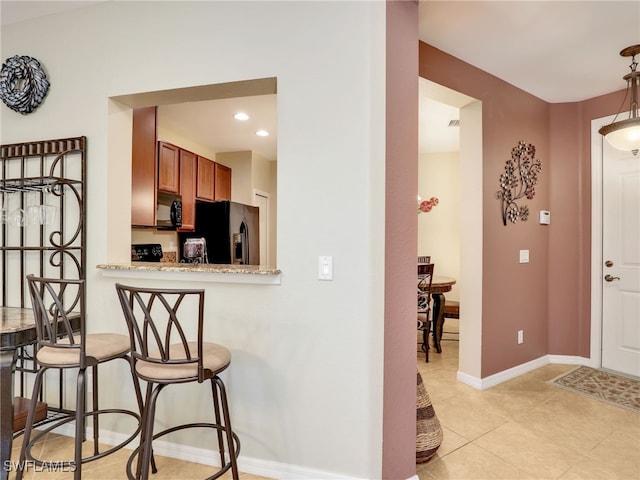 kitchen featuring light tile patterned floors, baseboards, a breakfast bar area, brown cabinets, and black appliances