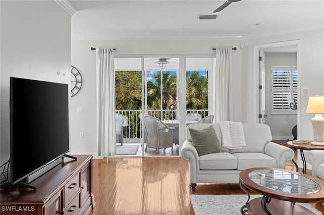 living area featuring visible vents, baseboards, wood finished floors, and crown molding