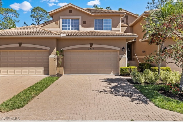 mediterranean / spanish-style house with stucco siding, a tile roof, and decorative driveway