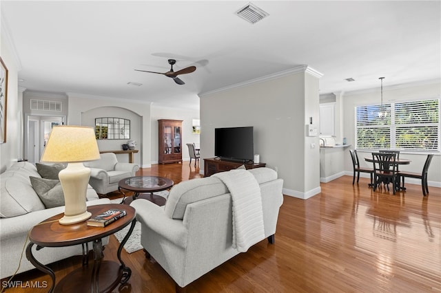 living area with visible vents, baseboards, ornamental molding, ceiling fan with notable chandelier, and wood finished floors