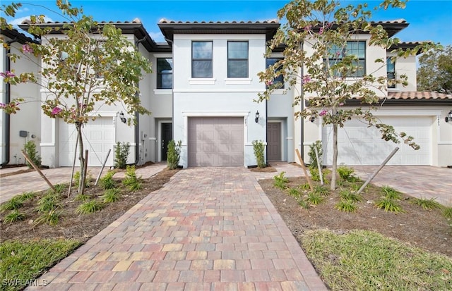 view of front facade with a tiled roof, decorative driveway, an attached garage, and stucco siding