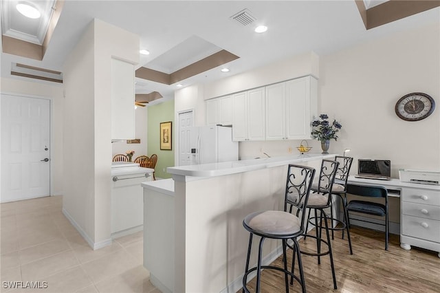 kitchen featuring visible vents, white refrigerator with ice dispenser, white cabinetry, a peninsula, and a breakfast bar area