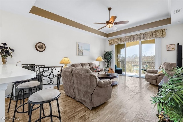 living area with visible vents, a raised ceiling, a ceiling fan, and wood finished floors