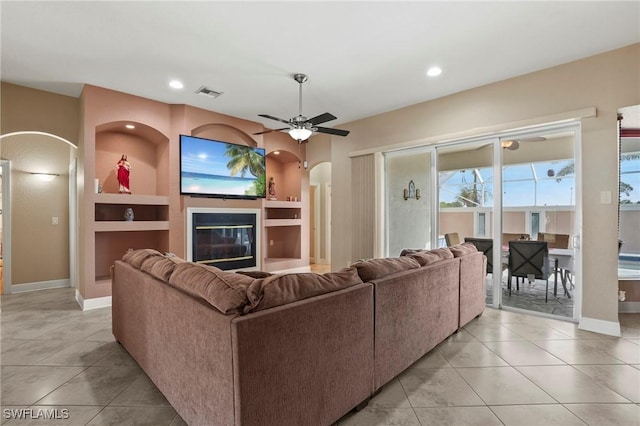 living area with a glass covered fireplace, visible vents, arched walkways, and ceiling fan