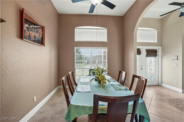 dining room with light tile patterned floors, a ceiling fan, baseboards, and a towering ceiling