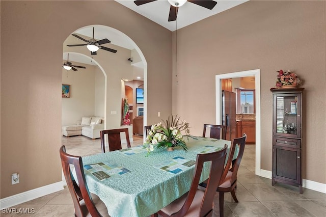 dining area with arched walkways, a high ceiling, light tile patterned floors, baseboards, and ceiling fan