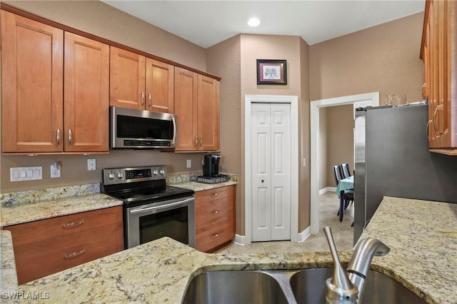 kitchen featuring light stone countertops, baseboards, a sink, stainless steel appliances, and brown cabinets