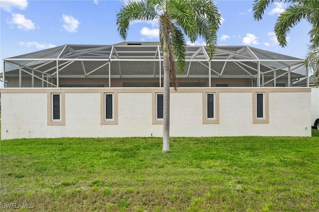 back of house with a lanai, stucco siding, and a lawn