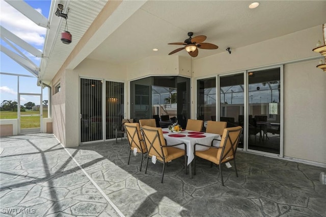 view of patio featuring glass enclosure, outdoor dining space, and ceiling fan