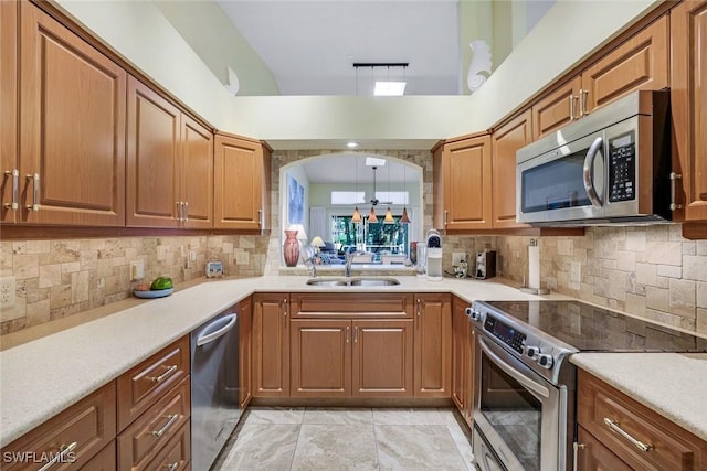 kitchen featuring appliances with stainless steel finishes, a sink, brown cabinetry, tasteful backsplash, and light countertops