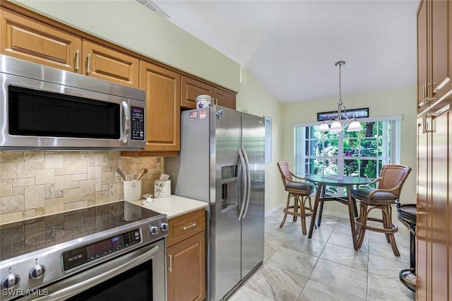 kitchen with appliances with stainless steel finishes, lofted ceiling, decorative backsplash, brown cabinetry, and a chandelier