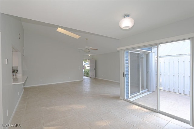 empty room featuring lofted ceiling, light tile patterned flooring, a ceiling fan, and baseboards