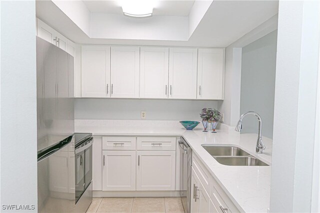 kitchen with light tile patterned floors, light stone counters, stainless steel appliances, a sink, and white cabinets