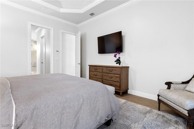 bedroom featuring wood finished floors, visible vents, baseboards, ornamental molding, and a tray ceiling