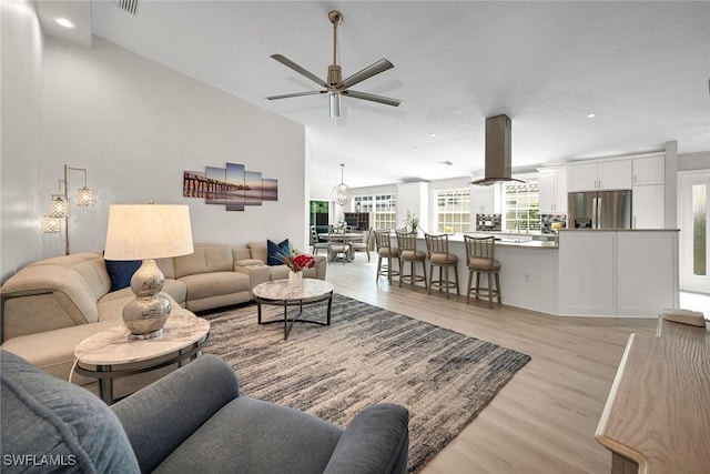 living area featuring visible vents, high vaulted ceiling, light wood-type flooring, and a ceiling fan