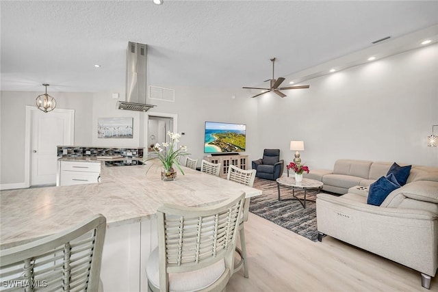 kitchen featuring open floor plan, wall chimney range hood, a kitchen breakfast bar, and light wood-style floors