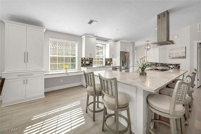 kitchen with stainless steel fridge, visible vents, island range hood, white cabinets, and a breakfast bar area