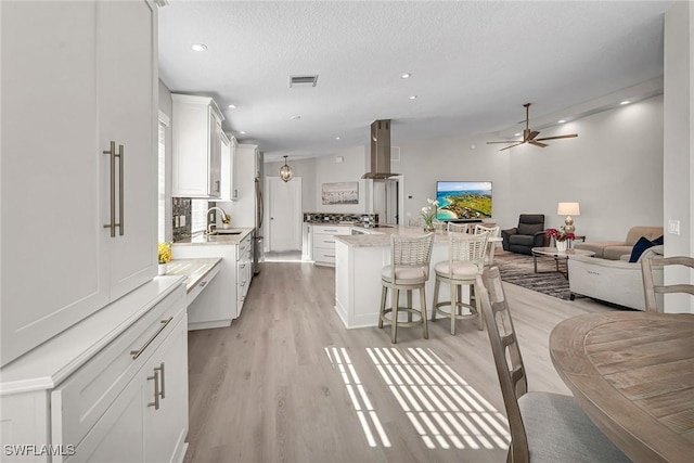 kitchen with visible vents, white cabinets, open floor plan, a sink, and exhaust hood