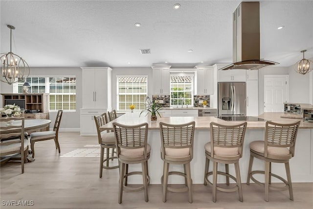 kitchen with island range hood, visible vents, white cabinets, stainless steel fridge with ice dispenser, and an inviting chandelier