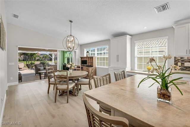 dining room with a chandelier, visible vents, light wood-style flooring, and a textured ceiling