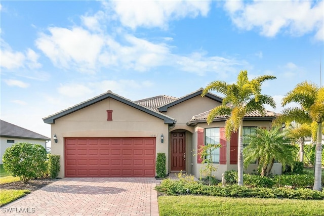 view of front of house with decorative driveway, an attached garage, a tile roof, and stucco siding