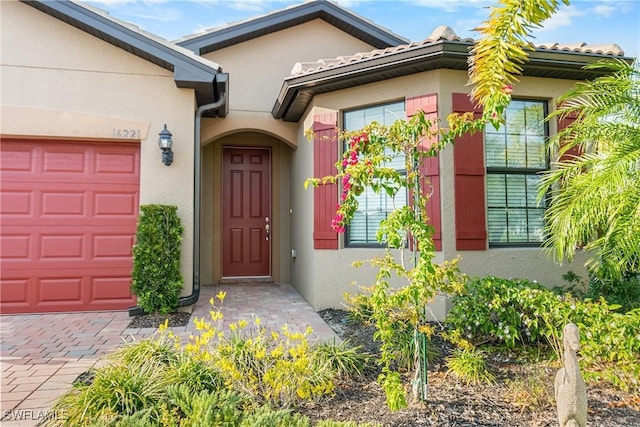 entrance to property with decorative driveway, an attached garage, and stucco siding