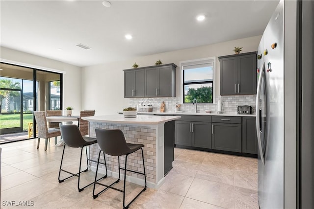 kitchen featuring a breakfast bar, a kitchen island, a sink, freestanding refrigerator, and decorative backsplash
