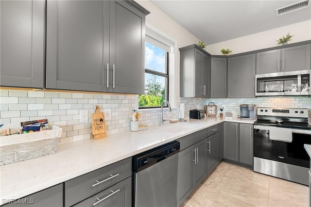 kitchen featuring visible vents, decorative backsplash, gray cabinetry, appliances with stainless steel finishes, and a sink