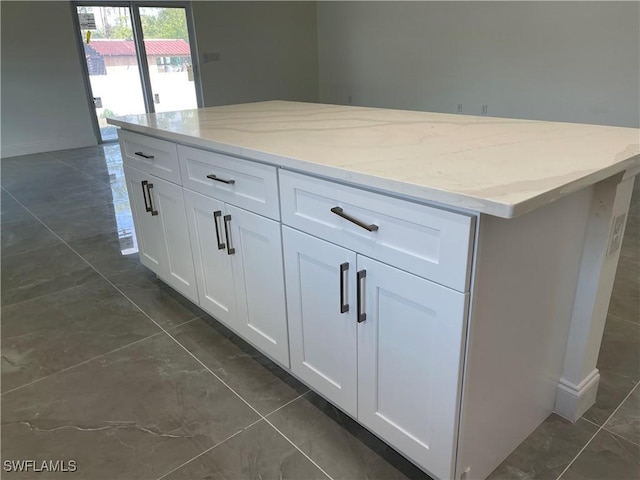 kitchen featuring light stone counters, baseboards, white cabinets, and a center island