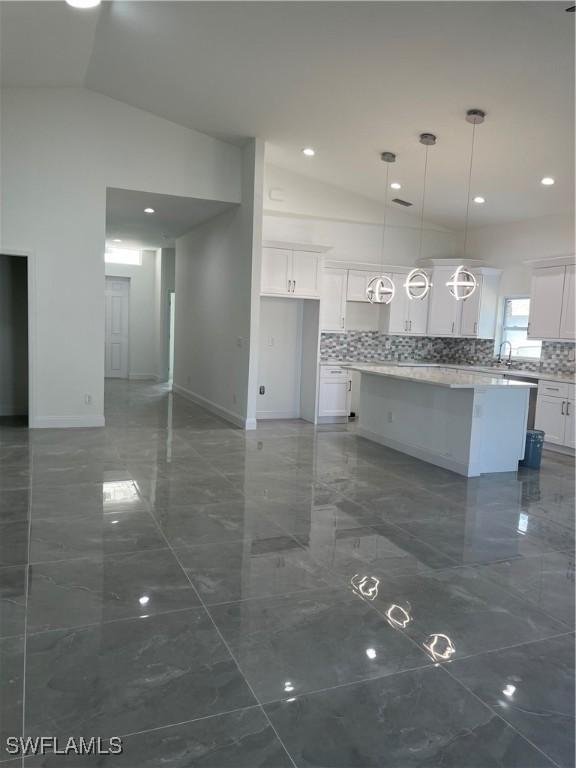 unfurnished living room with marble finish floor, baseboards, lofted ceiling, and a sink