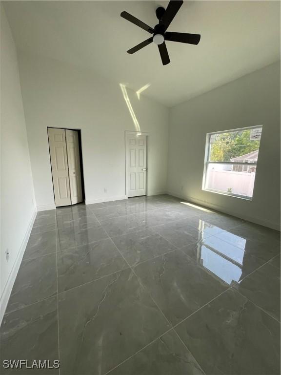 unfurnished room featuring marble finish floor, high vaulted ceiling, baseboards, and ceiling fan