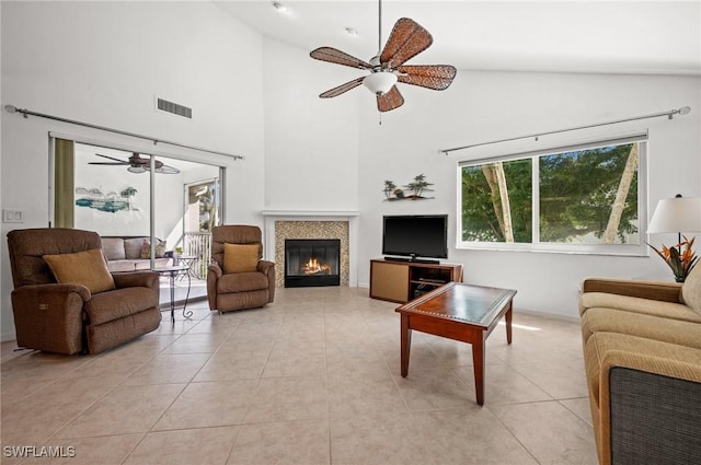 living room featuring light tile patterned floors, visible vents, a ceiling fan, and a glass covered fireplace