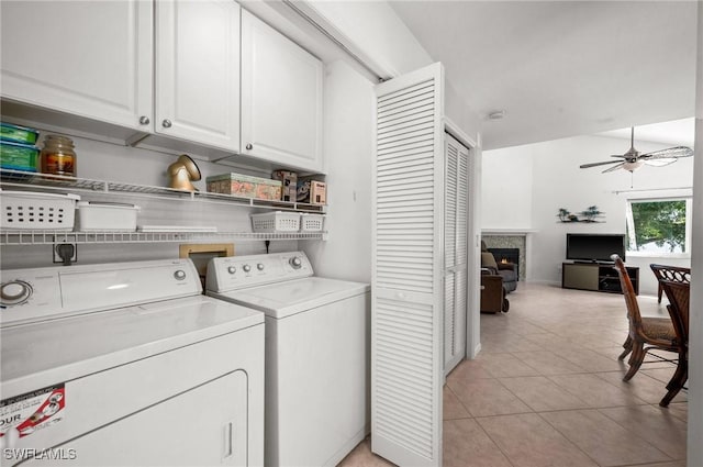 washroom with washer and clothes dryer, cabinet space, light tile patterned flooring, ceiling fan, and a warm lit fireplace