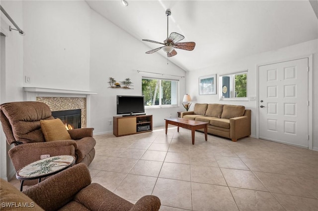 living area with light tile patterned floors, a tiled fireplace, a ceiling fan, high vaulted ceiling, and baseboards