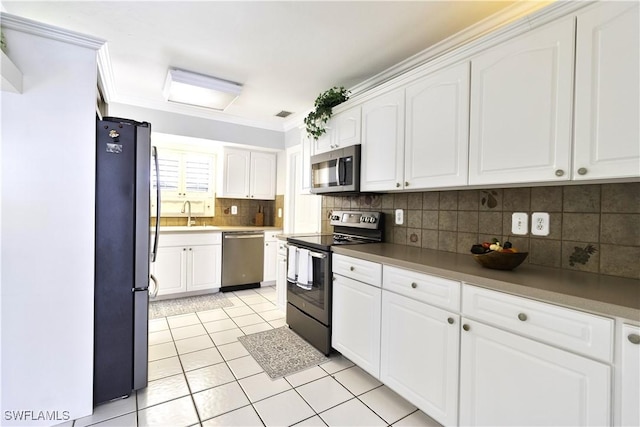 kitchen with tasteful backsplash, appliances with stainless steel finishes, crown molding, white cabinetry, and light tile patterned flooring