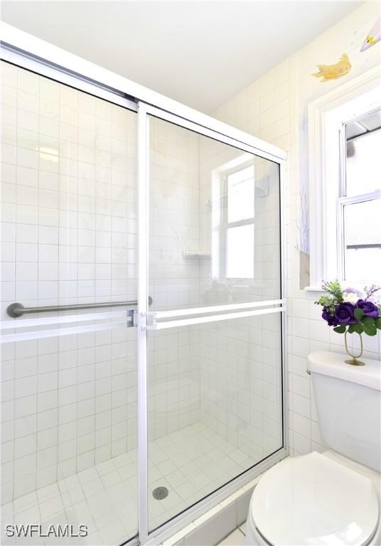 full bathroom with a stall shower, toilet, and tile walls