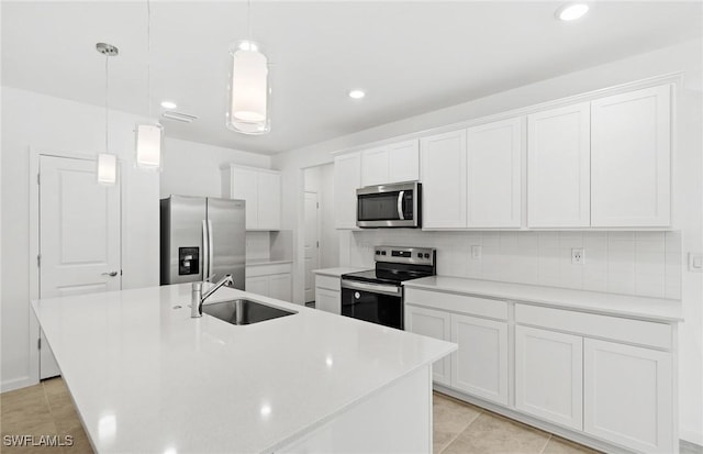 kitchen featuring appliances with stainless steel finishes, a sink, a kitchen island with sink, white cabinetry, and backsplash