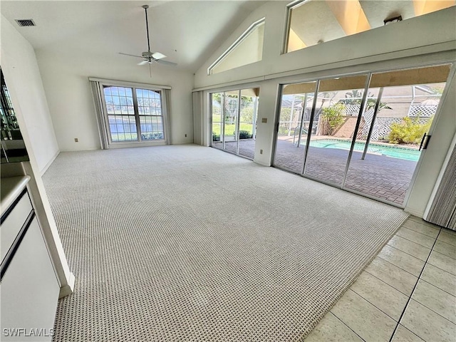 carpeted empty room featuring tile patterned floors, high vaulted ceiling, visible vents, and ceiling fan