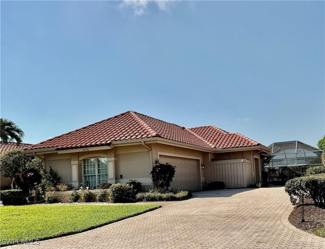 mediterranean / spanish house featuring a front yard, an attached garage, stucco siding, a tiled roof, and decorative driveway