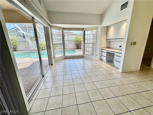 interior space featuring light tile patterned floors, baseboards, visible vents, and built in desk