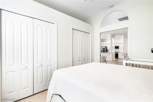 bedroom featuring light tile patterned floors, smart refrigerator, two closets, and visible vents