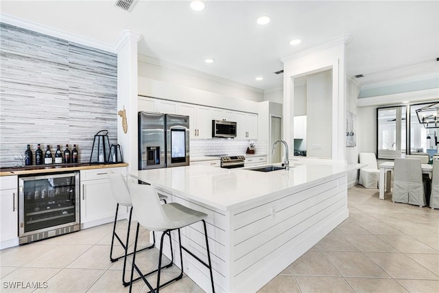 kitchen featuring light tile patterned floors, wine cooler, appliances with stainless steel finishes, a breakfast bar area, and a sink