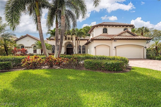 mediterranean / spanish home with decorative driveway, stucco siding, an attached garage, a front yard, and a tiled roof