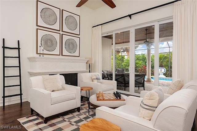 living area featuring a fireplace, baseboards, a ceiling fan, and wood finished floors