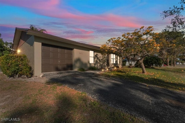 view of front of property featuring aphalt driveway, a lawn, a garage, and stucco siding