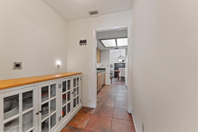 hallway with tile patterned floors, visible vents, and baseboards