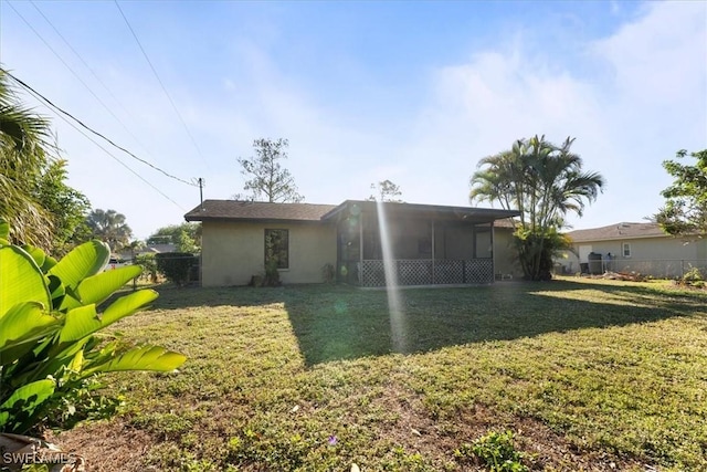 rear view of house featuring stucco siding, a lawn, fence, and a sunroom