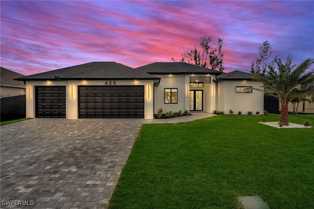 prairie-style home with a front lawn, decorative driveway, an attached garage, and fence