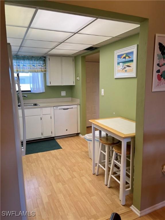 kitchen featuring a paneled ceiling, light countertops, dishwasher, and light wood-style flooring